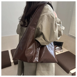 Borsa tote marrone scuro lucida a spalla su modella in un ufficio moderno minimalista