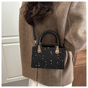 Detail of black crossbody bag with white star pattern and braided handle on model