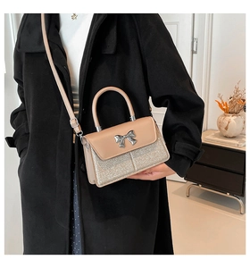 Detail of elegant apricot crossbody bag with silver glitter and bow clasp on black coat