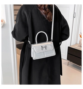 Detailed view of silver sequin crossbody bag with bow buckle decoration on black coat