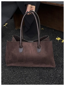 Detail view of large dark brown suede tote bag on autumn ground with ginkgo leaves