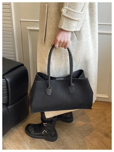 Matte black oversized tote bag held by a model in a beige coat for a minimalist chic look