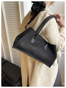 Model wearing a black matte tote bag with shoulder straps over a beige coat
