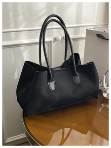 Detail of minimalist black matte leather tote bag with reinforced handles on a table