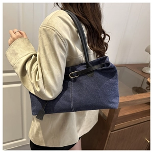 Dettaglio borsa tote in denim blu con manici in pelle nera e fibbia in metallo oro