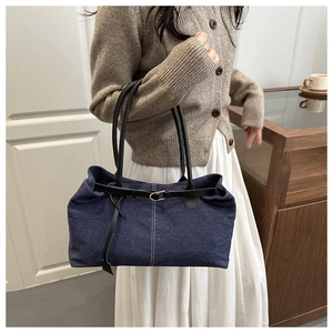 Dettaglio della borsa tote in denim blu con cinturini in pelle nera e fibbia in metallo
