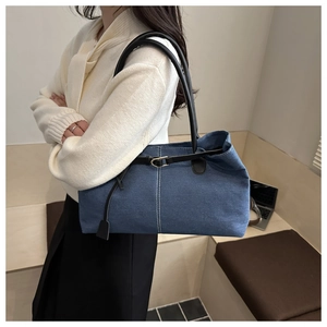 Dettaglio borsa tote in denim blu con cuciture bianche a contrasto e manici in pelle