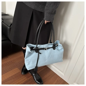 Dettaglio della borsa tote in tela azzurra con cinturini in pelle nera e ciondolo