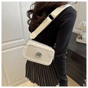 Detailed view of woven texture and silver M logo on cream crossbody bag with wide strap