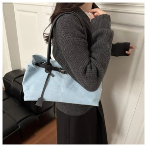 Dettaglio della borsa tote in denim azzurro con manici in pelle nera e ciondolo laterale