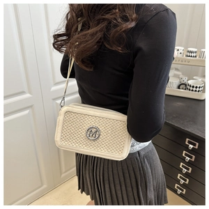 Detail of a beige woven crossbody bag with silver M logo and cream leather trim