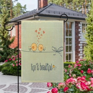 Close-up of linen garden flag with bird and heart motifs in a floral garden setting