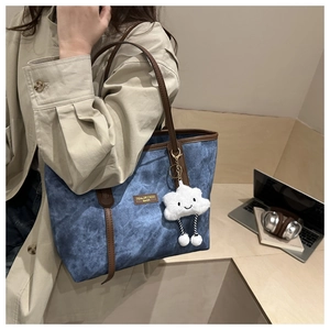 Detail of blue denim tote bag featuring brown leather straps and a fuzzy cloud charm