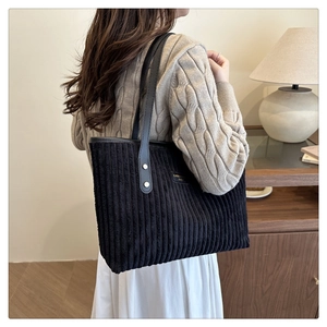 Dettaglio borsa tote in velluto a coste nero con manici in pelle e rivetti dorati