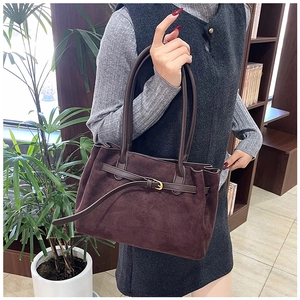 Detail of dark brown suede tote bag with metallic buckle straps and dual shoulder handles