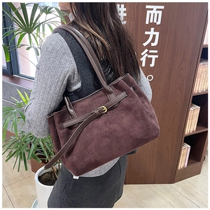 Detail of dark brown suede shoulder bag with gold buckle on a model in a library setting