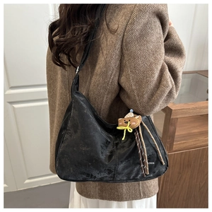 Detailed view of black hobo bag with vintage cracked texture and teddy bear pendant