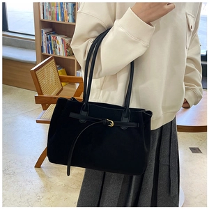 Detailed view of black suede tote bag with gold buckle and long shoulder strap in context