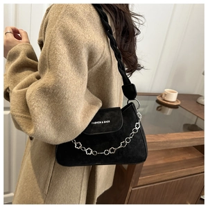 Close-up of black suede underarm bag with silver floral chain and woven strap detail