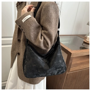 Close-up of black crescent shoulder bag with matte texture on model's wool coat