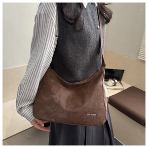 Détail du sac hobo en daim marron avec logo Tidal Dryness porté à l'épaule
