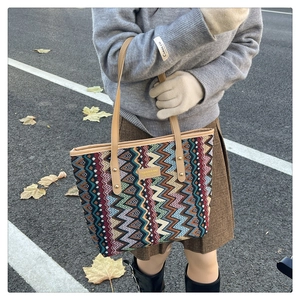 Outdoor shot of a woven tote bag with colorful wave patterns and brown leather handles
