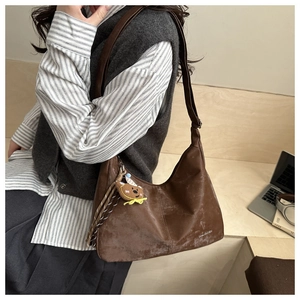 Detail of a large brown vintage PU leather tote bag with vertical stitching and bear charm