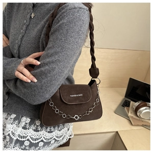 Detail of brown woven strap underarm bag with decorative floral metal chain