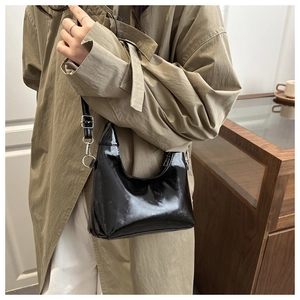 Borsa sottobraccio nera lucida con fibbie argento indossata su un trenchcoat