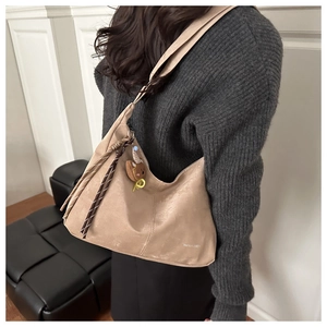 Detail view of large beige tote bag with fringe charm and bear plushie on shoulder