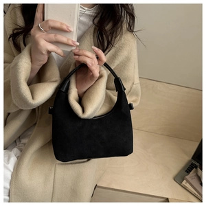 Dettaglio borsa hobo nera in camoscio con manico curvo abbinata a un cappotto beige