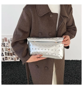 Close-up of silver metallic clutch bag with rivet studs held by model in wool coat