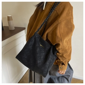 Detail of black suede tote bag featuring woven shoulder strap and golden logo text