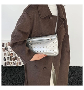 Detail of silver metallic clutch with punk rivets held by a model in a wool coat