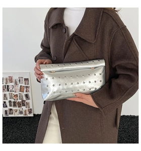 Detail of silver metallic clutch bag with rivet studs held by model in tweed coat