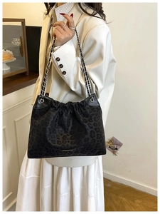 Detail of black leopard print tote bag with chain strap and gold logo against white blazer