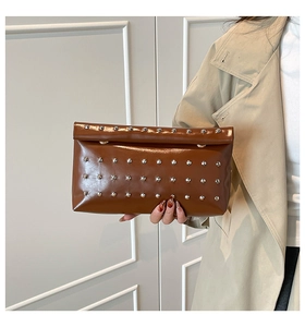 Detail view of brown glossy leather envelope clutch with silver rivets on model
