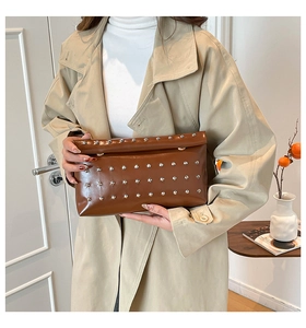 Detail of dark brown rivet clutch bag held by a model in a stylish trench coat