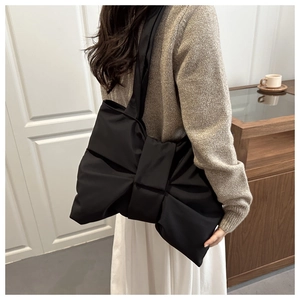 Dettaglio di una borsa a tracolla con fiocco nero che mostra la trama in raso e il design ampio