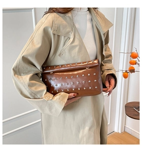 Detail of dark brown glossy leather clutch with silver studs held by a model