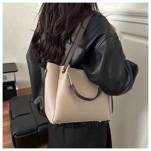 Dettaglio della borsa a secchiello in pelle beige con finiture dorate su una modella