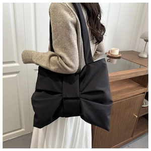 Dettaglio di una borsa tote in nylon nero a forma di fiocco indossata da una modella in interno