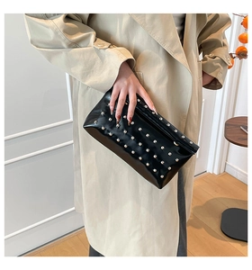 Détail d'une pochette en cuir verni noir ornée de clous métalliques argentés chic