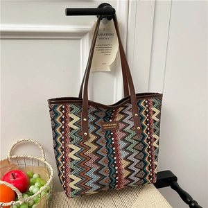 Ethnic style tote bag with colorful wave patterns and brown leather handles on a white wall