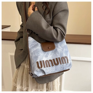 Detail of blue denim tote bag with brown leather patchwork and large letter embroidery