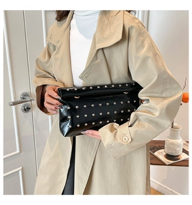 Detail of a black patent leather clutch with silver rivets held against a beige coat