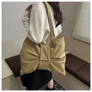 Modella che indossa una borsa a tracolla kaki oversize con fiocco su sfondo minimalista