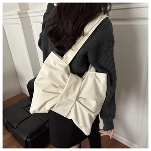 Dettaglio di una borsa a tracolla beige a forma di fiocco con morbida trama su una modella
