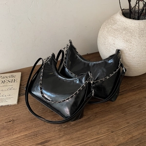 Borsa hobo minimalista in pelle lucida nera con catena d'argento su sfondo in legno