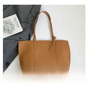Detail of a large brown leather tote bag with gold logo lettering on white background